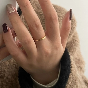 Close-up of a slender gold bird ring with a tiny crystal on a finger wearing a brown coat