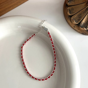 Detail of red braided rope bracelet with silver beads and lobster clasp on ceramic plate