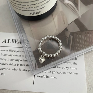 Vue détaillée d'une bague en perles argentées avec pendentif cœur poli sur fond minimaliste