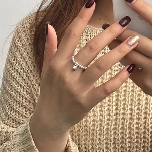 Gros plan d'une bague perlée en argent S925 avec pendentif cœur au doigt