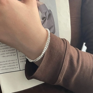 Detailed view of layered S925 silver chain and mini pearls worn on a woman's wrist