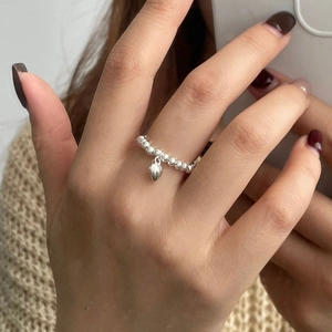 Gros plan détaillé d'une bague à perles et cœur en argent avec un pull beige