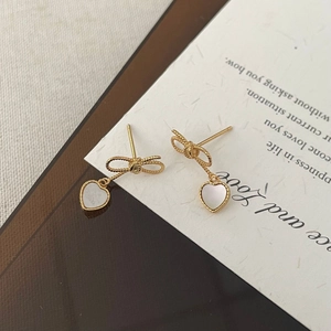 Détail des boucles d'oreilles nœud dorées avec pendentifs cœur en nacre élégants