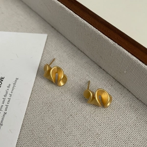 Macro shot of matte gold lotus petal earrings with 3D folded geometry on linen tray