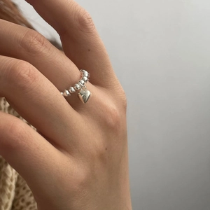 Gros plan détaillé d'une bague perlée en argent avec pendentif cœur élégant au doigt