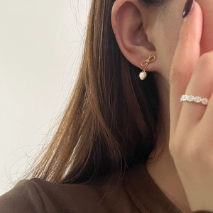 Gros plan de boucles d'oreilles nœud doré et d'une bague délicate portées par un mannequin