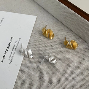 Detail of matte silver and gold ruffle earrings showcased on a textured grey tray