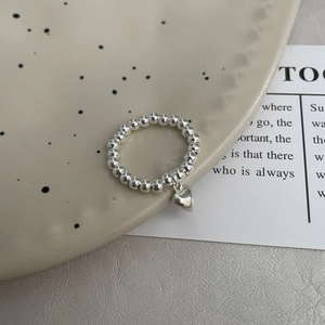 Détail de la bague en argent 925 avec perles et breloque cœur sur un plateau en céramique