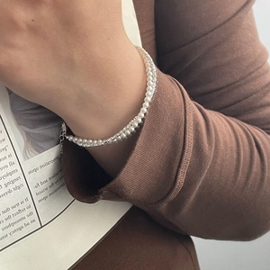 Detailed macro view of S925 silver pearl wrap bracelet on wrist with elegant knit sleeve