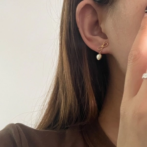 Boucles d'oreilles nœud dorées avec pendentifs cœur en nacre portées par mannequin