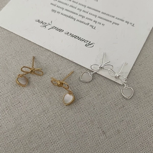 Vue détaillée de boucles d'oreilles nœud et cœur avec nacre sur lin beige
