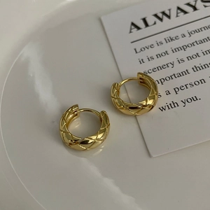 Close-up of golden checkered pattern earrings on a minimalist white ceramic tray