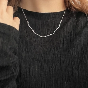Close-up of minimalist S925 sterling silver wavy beaded necklace on black knitwear