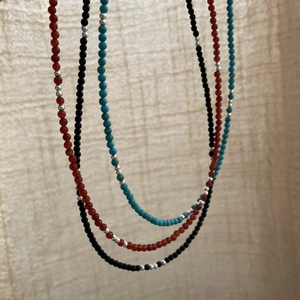 Détail de colliers en argent S925 avec perles en pierres naturelles rouges, noires et bleues