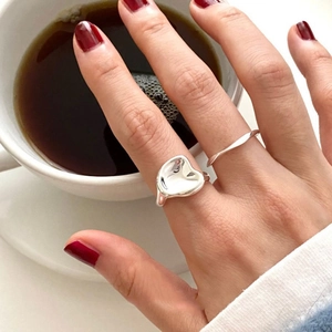 Nahaufnahme von S925 Silberringen mit Wellentextur auf der Hand an einer weißen Kaffeetasse
