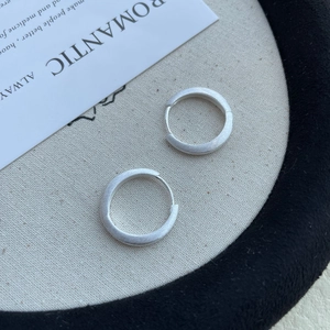 Detailed close-up of matte brushed S925 silver hoop earrings on beige textured fabric