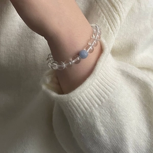 Détail d'un bracelet en perles de cristal clair avec pierre bleue sur pull blanc