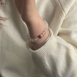 Detail of white crystal beaded bracelet with red agate bead and silver bangle on wrist