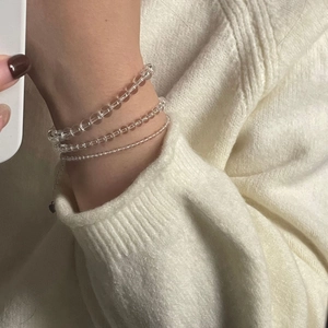 Close-up of three layered white crystal beaded bracelets on a soft knit sweater sleeve