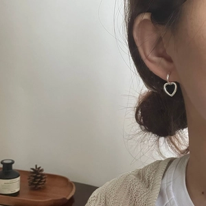 Close-up of minimalist sterling silver heart dangle hoop earrings on a female model