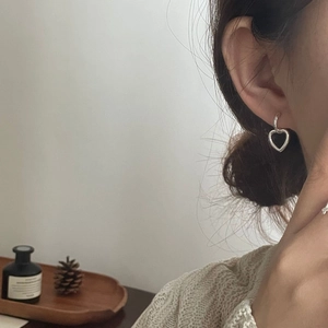 Detail of 925 sterling silver heart-shaped hoop earrings worn by a model in warm light
