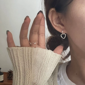 Close-up of a silver heart-shaped drop earring and a gold bow ring worn by a woman