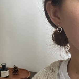 Detail view of a 925 sterling silver heart-shaped pendant hoop earring on a model ear