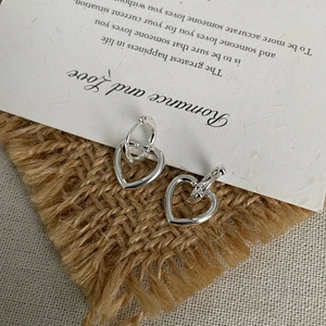 Macro detail of silver heart hoop earrings on minimalist paper with poetic text