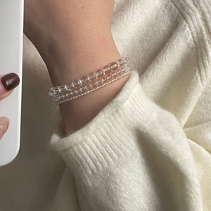 Detailed view of the triple-layer clear crystal bead bracelet worn on a white sweater