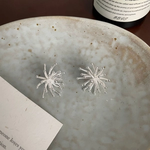 Detailed view of silver starburst earrings with bead tips on a grey ceramic tray