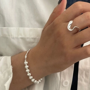 Detail of minimalist wavy silver ring and beaded bracelet on a white shirt background