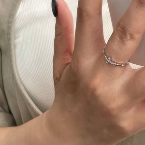 Macro shot of minimalist silver cross star ring on finger with white knit background