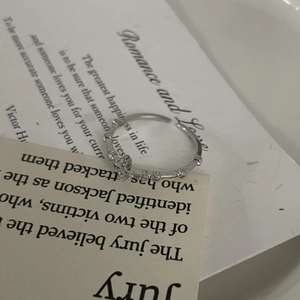 Detail shot of a silver adjustable cross ring with small crystals on a paper background