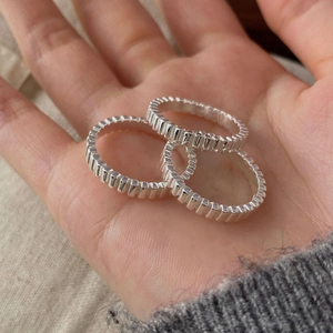 Detail shot of three S925 sterling silver rings with vertical gear texture held in palm