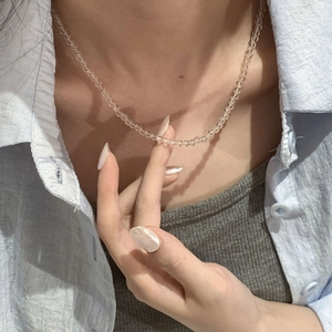 Gros plan d'un collier en cristal blanc transparent porté avec une chemise bleu clair
