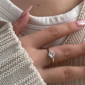 Gros plan d'une bague géométrique en argent avec zircon carré sur une main de femme