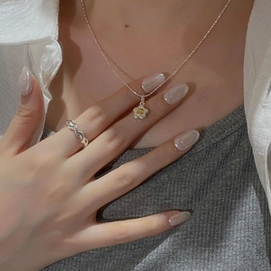 Detail of silver sun flower necklace and wavy ring styled on a layered outfit