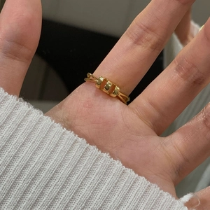 Detail of a minimalist gold geometric ring featuring three square elements on a split band