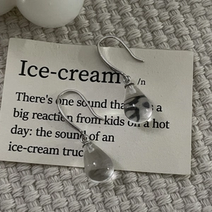 Macro shot of silver drop earrings with clear crystal glass on a beige knit fabric