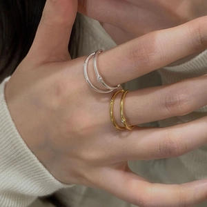 Detailed view of silver and gold double-layered rings with a small zircon on a white sweater