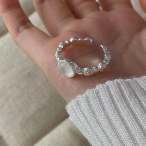 Dettaglio dell'anello a onde in argento S925 con gemma lattea tonda sulla mano