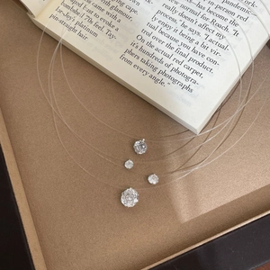Detail of four invisible fishing line necklaces with round-cut pendants on a velvet tray