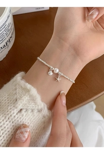 Detail of silver starfish and shell bracelet with pearls worn on wrist for a chic look