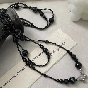 Detail of layered black onyx bead necklace with silver accents on artistic stone background