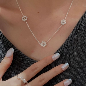 Détail du collier fleur en perles et bague en argent portés par un mannequin en maille