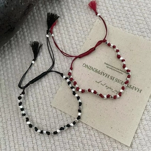 Détail de bracelets tressés rouges et noirs avec des perles en argent et des glands