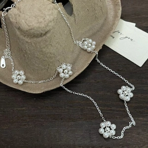 Détail macro d'une chaîne en argent 925 avec cinq breloques fleurs en perles blanches
