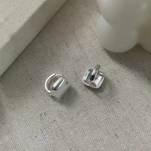 Macro shot of minimalist square silver geometric hoop earrings on textured grey fabric