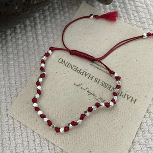 Détail du bracelet en corde tressée rouge avec perles argentées et pompons