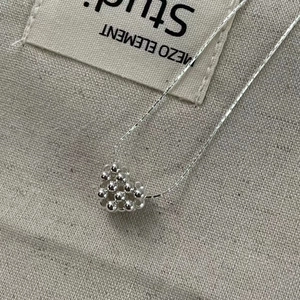 Gros plan du pendentif cœur en perles d'argent S925 avec chaîne fine sur tissu gris